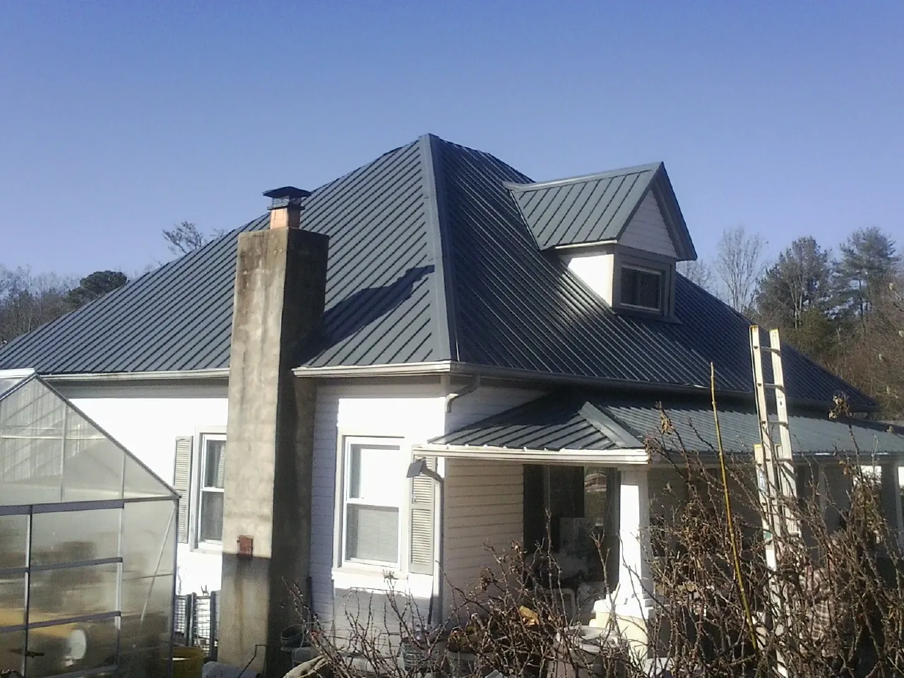 Dark blue standing seam metal roof on a white farmhouse with dormer — Slate & Tile Roof Repair by Roofing Brothers in Pearl