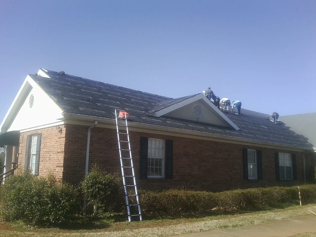 Crew tearing shingles off a brick ranch roof with a ladder set — Emergency Roof Repair work by our crew in Pearl