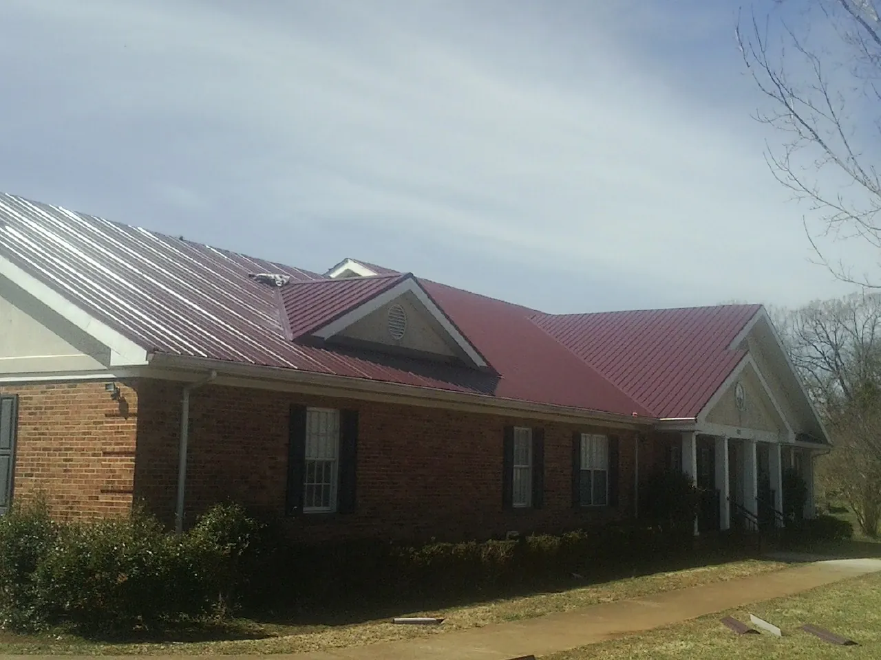 Red metal roof with gabled entries on a long brick building, from a Hail Damage Roof Repair job in Pearl