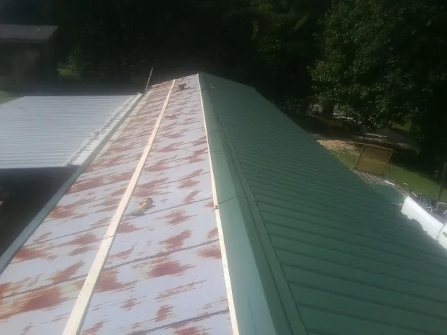 Old rusted panels beside newly installed green metal roofing — Wind Damage Roof Repair by Roofing Brothers in Pearl
