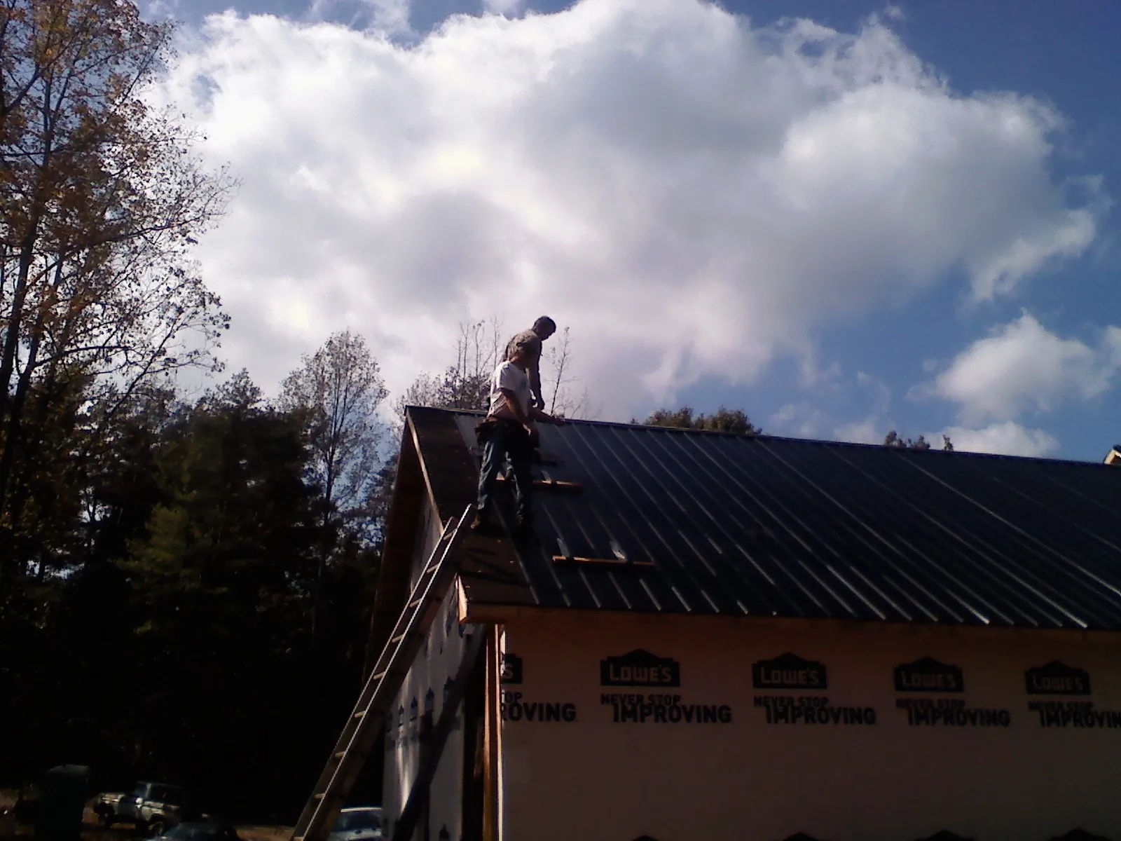 Roofer fastening dark metal panels high against a cloudy sky, from a Roof Inspection job in Pearl