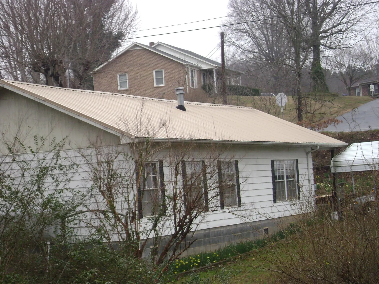 Tan metal roof on a white sided house set into a hillside — Commercial Roofing by Roofing Brothers in Pearl