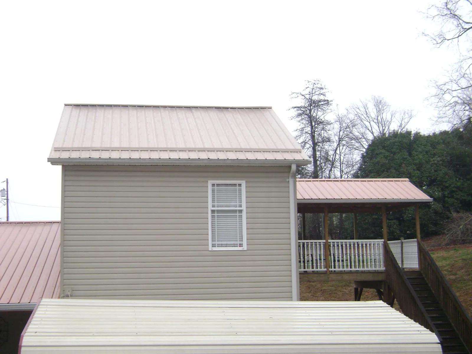 Tan metal roofs on a two story addition and attached porch, from a Roof Replacement job in Pearl